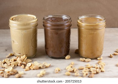 Peanut butter, hazlenut spread, and cashew butter on a wooden table.