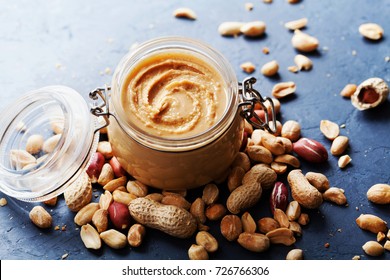 Peanut butter jar and heap of nuts on dark rustic background.