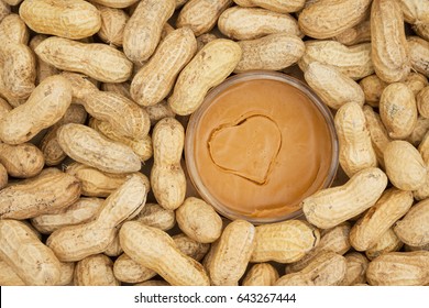 Peanut Butter In A Jar With Heart Shape And Raw Peanuts In Shells Background