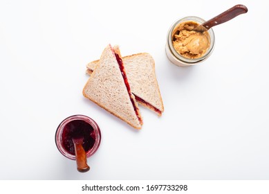 Peanut butter and jelly sandwich halves and glass jars on a white background, top view