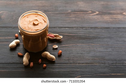 peanut butter on a table in a glass jar with peanuts around