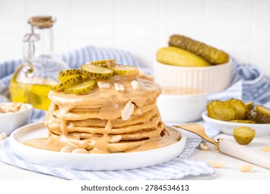 Peanut butter Pickle Pancakes. Stack of fluffy tasty savory Pancakes wit a lot of Peanut butter drizzle, peanuts and pickles, copy space