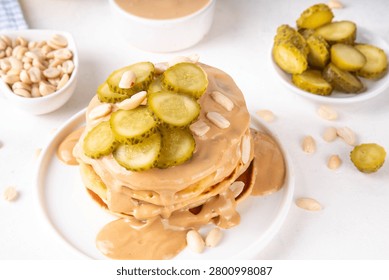 Peanut butter Pickle Pancakes. Stack of fluffy tasty savory Pancakes wit a lot of Peanut butter drizzle, peanuts and pickles, copy space