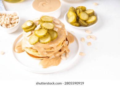 Peanut butter Pickle Pancakes. Stack of fluffy tasty savory Pancakes wit a lot of Peanut butter drizzle, peanuts and pickles, copy space