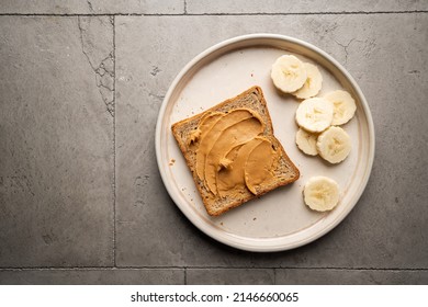 Peanut Butter Toast With Banana Slices On Ceramic Plate. Healthy Breakfast Or Snack On Grey Concrete Background., Top View