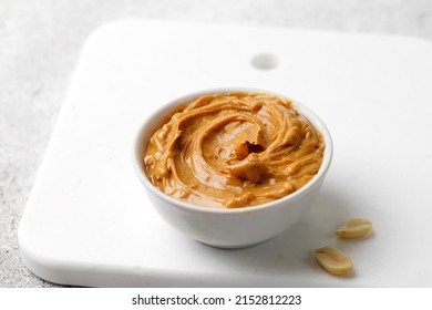 Peanut Butter In A White Saucer On White Board. Curl Of Peanut Butter With Peanut. Copy Space