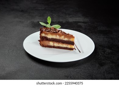Torta de cacahuete y caramelo con chocolate sobre un plato blanco sobre fondo de piedra oscura. Un trozo de tarta de Snickers con un estilo mínimo. Café, nueces y pastel de chocolate en la carta de repostería