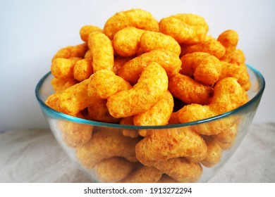 peanut flips . lots of corn sticks in peanut glaze in a glass round bowl on a gray light background with a white wall side view