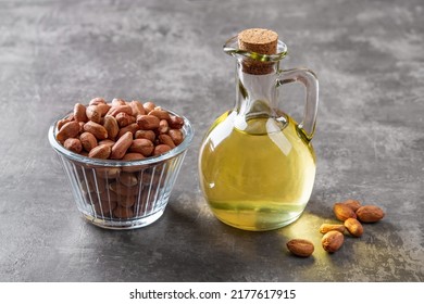 Peanut oil in a glass jug and raw peeled groundnut in a glass bowl over gray background. Arachis hypogaea as edible seeds and oil crop. Monounsaturated cooking oil. Vegetarian snack. Top view.