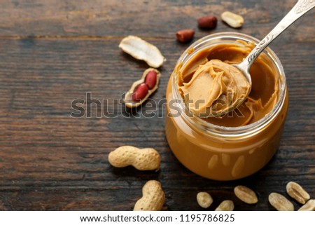 peanut paste in an open jar and peanuts in the peel scattered on the table
