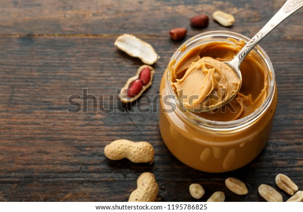 peanut paste in an open jar and peanuts in the\
peel scattered on the\
table\

