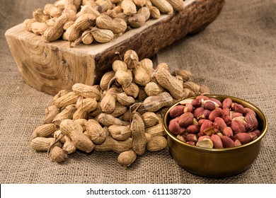 Peanuts in nutshell on a piece of wood and peeled peanuts in golden bowl on sackcloth