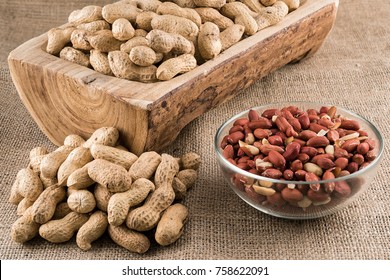 Peanuts in nutshell on a piece of wood and peeled peanuts in a bowl on sackcloth