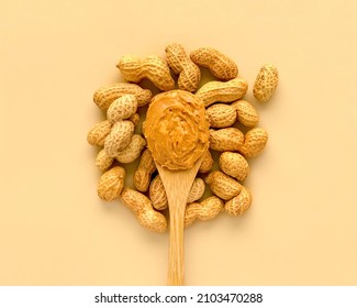 Peanuts and peanut butter in wooden bamboo spoon on beige background