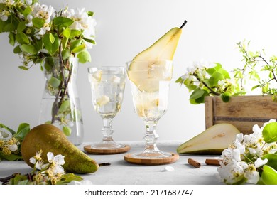 Pear cocktail with pear puree and fresh fruit and flowers on light gray background. Summer cold pear drink lemonade with ice on the table, Sparkling Mocktail dessert beverage with flowering twigs