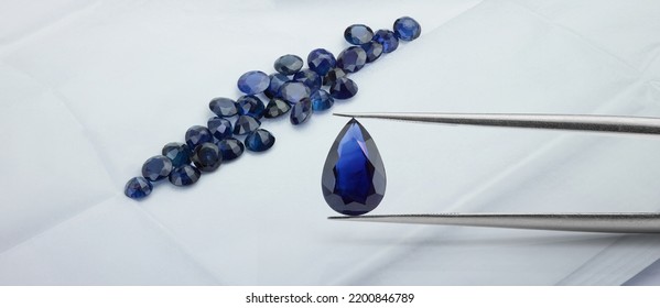 Pear Shaped Blue Sapphire Held in Tweezers Over Parcel of Blue Sapphire Gemstones. Wide Banner Sized Photograph. - Shutterstock ID 2200846789