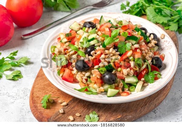 Pearl barley salad with vegetables\
in a plate close-up. Boiled pearl barley with tomatoes, cucumbers,\
olives, parsley and basil. Vegan and vegetarian\
food.
