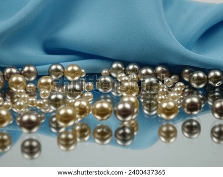 Pearl beads of various colors lie on the mirror and are reflected in it against the background of blue satin fabric.