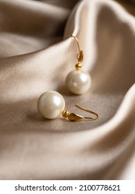 Pearl earrings with golden fittings on shiny beige silk background. Beautiful accessories for women. Elegant jewelery gift or present for wedding or saint valentine's day.