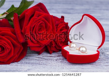 Pearl earrings in jewelry box and red roses. Red blooming roses and a box with gold jewelry on wooden background. Valentines Day, Birthday or marriage concept.