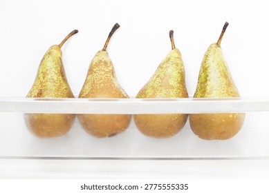 Pears inside fridge background. Four ripe fruits aligned. Refrigerator drawer storage detail. Yellow green pear texture. Kitchen organization food scene. Healthy natural produce closeup.