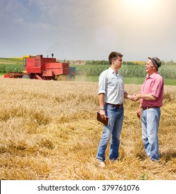 Peasant and businessman shaking hands on wheat field