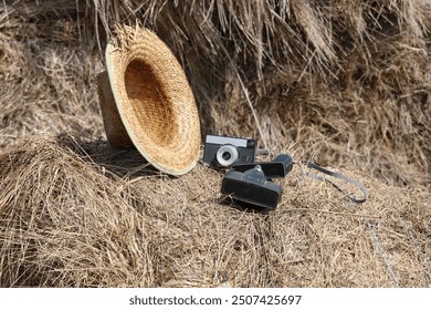 A peasant straw hat and an old camera, placed on a bale of straw from a larger pile.
