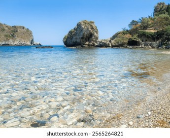 Pebble beach and clear blue water near Isola Bella, Taormina. The rocky coastline and calm sea create a tranquil Mediterranean retreat. Sicily, Italy. Copy space. - Powered by Shutterstock