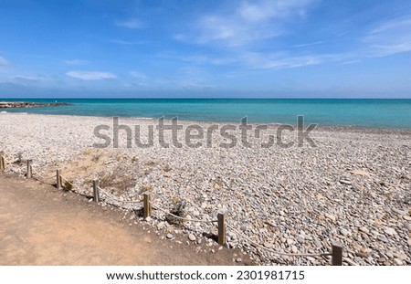 Pebble stone beach. Sea beach shore with waves in ocean. Waves in sea near coastline on empty pebble beach. Sea beach landscape. Coast pebbles. Shore landscape on Spain resort. Ocean shoreline scenic.