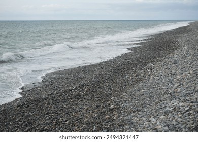 pebble stones by the sea. Silky blue waves of Black sea. Coast. Waves and round pebbles on ocean beach. Turquoise water and sea foam. - Powered by Shutterstock