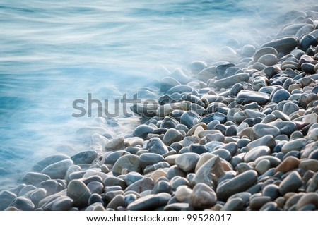 pebble stones by the sea. Silky waves of blue sea from long exposure.