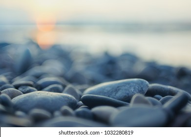 Pebble stones on the shore close up in the blurry sunset light in the distance  background. - Shutterstock ID 1032280819