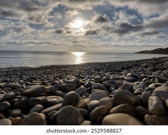 Pebbled beach, calm sea, sun-kissed water. Dramatic clouds, contrasting sky. Tranquil coastal scene. - Powered by Shutterstock