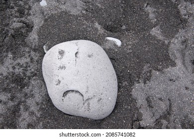 Pebbles On The Black Sand Beach, Basalt Beach Of Jökulsárlón A Glacial Lake In Southeast Iceland Near Höfn. This Stone Looks Like A Sad Or Bitter Face.