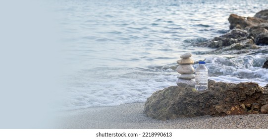 pebbles in pyramid one over another   bottle and drinking water big rock beach sea waves in background pure water bottle   stones surrounded by water wave beach sand wide banner free space 