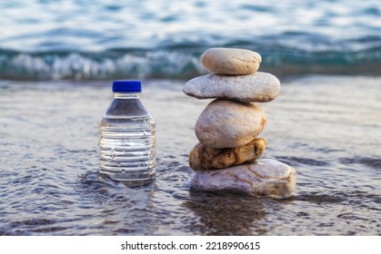 pebbles in pyramid one over another   bottle and drinking water big rock beach sea waves in background pure water bottle   stones surrounded by water wave beach sand wide banner free space 