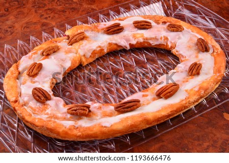 Pecan Kringle oval with pecans on top laying on a clear tray over a burl countertop. 
