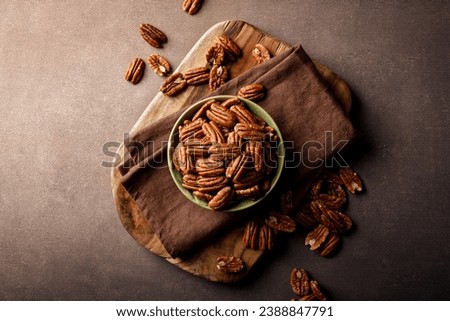 Pecan nuts in a bowl on a brown background, top view