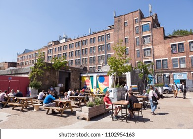 PECKHAM, UK - MAY 19, 2018: People drinking and hanging around outside a bar in the trendy Copeland Park in South London. The Bussey Building is in the background.