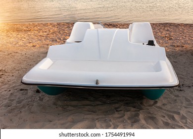 Pedal boats on the sunset on a tropical island beach. White catamaran on an empty sea shore on evening landscape with sun rays. Wallpaper for desktop, poster, marine travel photo, post card design.