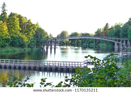 Pedestraiins bridge over the river surrounded by green trees in the evening sun light in Latvia Ogre city.