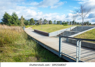 Pedestrian boardwalk footpath in a suburban park leads to a neighborhood with some modern Australian houses in the distance. Concept of the public green land in the suburb and the local park.