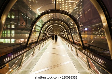 pedestrian bridge with glass dome in La Defense, Paris, at night, and walking business people in motion blur