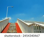 Pedestrian bridge with white railing and rusty stairs and blue sky