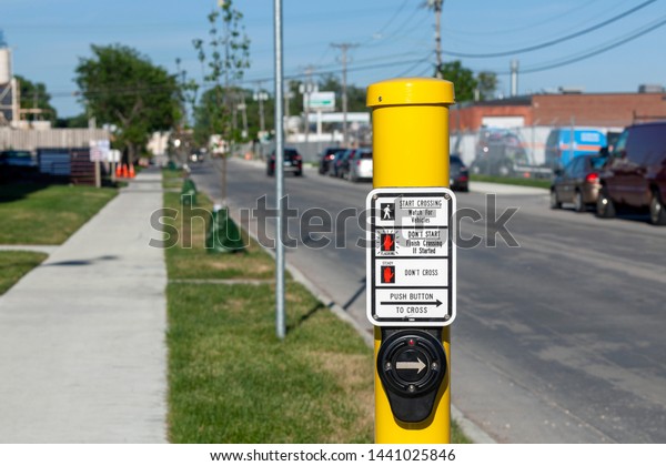 Pedestrian crossing call button with blurred\
background of street and\
cars.