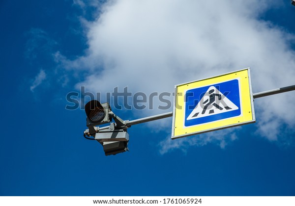 Pedestrian crossing sign and traffic\
light on cloudy sky background, traffic safety\
concept.