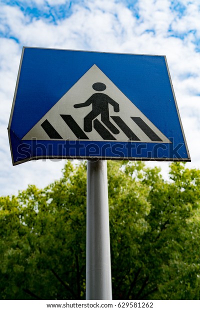 pedestrian sign or crosswalk sign with blue sky and\
green tree