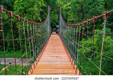 Pedestrian suspension bridge with a blur foreground of the closest steel thread handrails and wooden path
