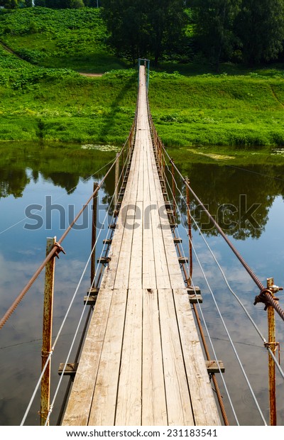 Pedestrian suspension bridge of steel and wood\
over the river, summer in\
Russia