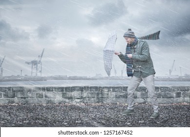 Pedestrian With An Umbrella Is Facing Strong Wind And Rain On A Dockside